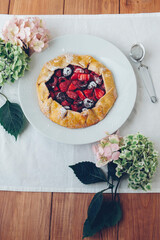 Delicious freshly baked vegan strawberry and cherry galette on wooden rustic background with hydrangea flowers. Sweet food, summer dessert.