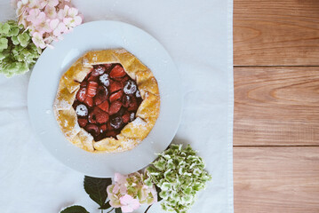 Delicious freshly baked vegan strawberry and cherry galette on wooden rustic background with hydrangea flowers, top view. Sweet food, summer dessert.