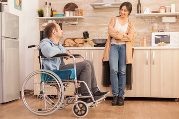 Woman smiling at disabled husband in wheelchair while talking with him. Disabled paralyzed...