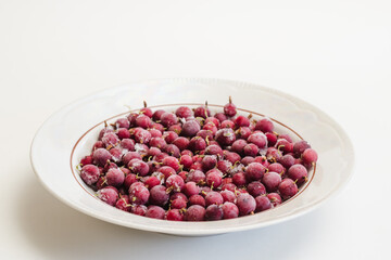 White plate with frozen red gooseberries covered with hoarfrost on white background