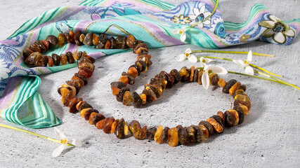 Amazing glittering dark green and orange amber necklace on a green silk scarf. Amber jewelry with snowdrops on a gray background. Retro composition. 