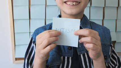 Autism awareness concept. Autism boy with glasses front a board with stickers and holds the note Autism.
