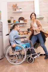 Disabled man in wheelchair singing with his wife in kitchen. Young couple having fun.