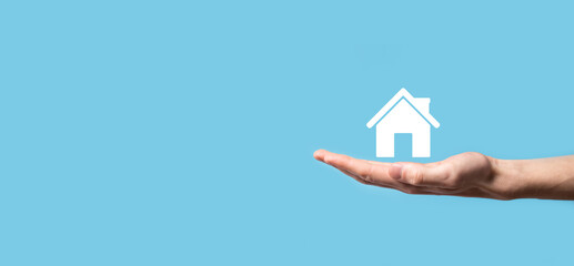 Naklejka premium Male hand holding house icon on blue background. Property insurance and security concept.Real estate concept.