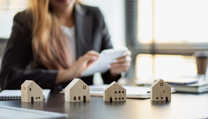 Close up wooden toy house with business woman signs a purchase contract or mortgage for a home,...