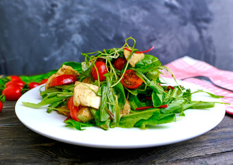 Fresh salad with fresh herbs, cherry tomatoes, soft Italian cheese on a plate. A delicious and healthy meal.