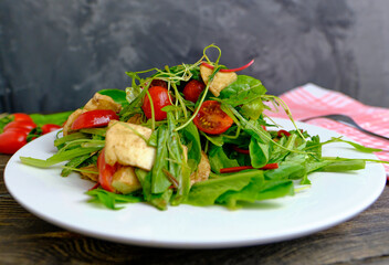 Fresh salad with fresh herbs, cherry tomatoes, soft Italian cheese on a plate. A delicious and healthy meal.