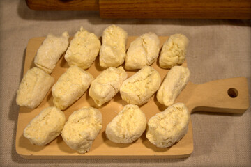 The process of making dumplings in the home kitchen. Pieces of raw dough are placed on a wooden board on linen cloth. Nearby is an old wooden rolling pin and a couple of chicken eggs.
