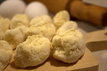 The process of making dumplings in the home kitchen. Pieces of raw dough are placed on a wooden board on linen cloth. Nearby is an old wooden rolling pin and a couple of chicken eggs.