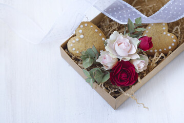 cookies in the shape of a heart and small roses in a box on a light background