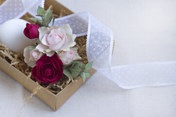 in the box: small red and pink roses, eucalyptus leaves, egg, ribbon. postcard for Easter.