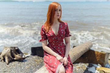 Young redhead woman in white dress enjoys sea.