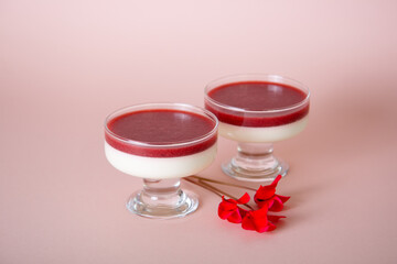 Strawberry Pannakotta in a glass decorated with fresh flowers on pink background.