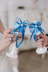 Wedding day. Hands of the bride and groom are holding wedding glasses with champagne, decorated in blue colors. Blue bow on the glass. Close-up. Details of the wedding.