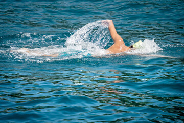 Male freestyle swimmer (front crawl) in the blue waves of the Mediterranean sea, side view.