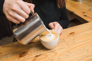 Fototapeta na wymiar Woman barista makes coffee, pours milk into cappuccino coffee