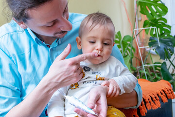 Father rubbing pain relieving gel into his little baby boy's growing teeth or gums.  Baby...