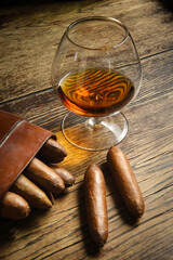 short cigars on a wooden table inside a leather cigar case and a glass of cognac