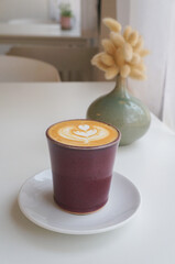 Heart shaped hot coffee latte art in a mug placed on a white table.