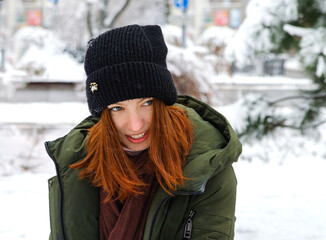 A red-haired girl in a green jacket against the snow. A walk in winter. Playing with snow