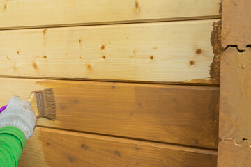 A worker's hand in a glove, painting a wooden house. Covering a wooden house with a protective compound.