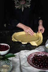 Step by step process of making cherry custard pie. Woman in black dress spreading dough in bio baking form.