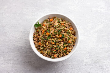Delicious vegetarian buckwheat with cabbage, carrots, onions, nuts and herbs on a light gray textured background, top view. Homemade diet healthy food