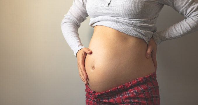 Pregnant woman holding her big naked belly with her hands. Maternal prenatal care. Maternity, pregnancy, baby expectation concept. Second trimester of pregnancy. Copy space