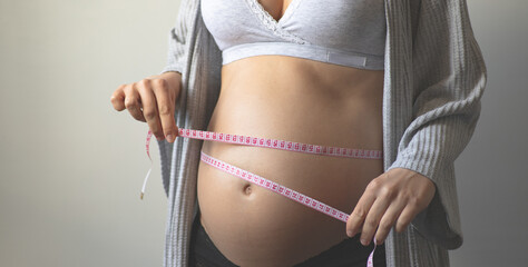 Pregnant woman measuring the volume of her pregnant belly with a measuring tape. Health and weight gain during pregnancy. Maternal prenatal care. Maternity, pregnancy, baby expectation concept