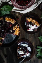 Cut homemade cherry and custard pie and pieces of with ice cream on glass plate on dark wooden table.