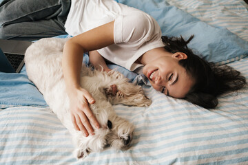 Happy white woman stroking her dog while lying on bed at home