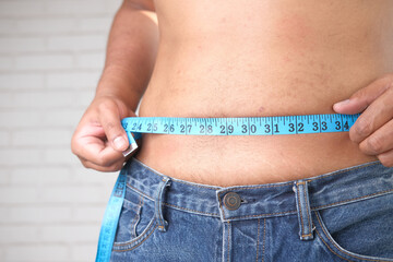 young man measuring his waist with a tape measure, close up.