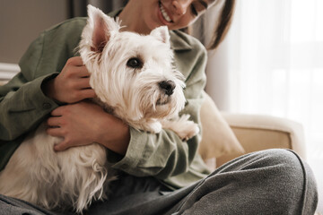 Happy white woman stroking her dog while sitting on sofa at home