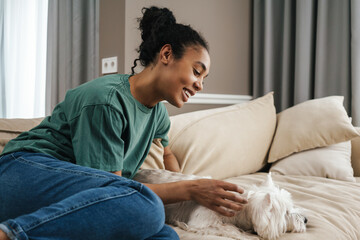 Happy black woman stroking her dog while resting on sofa at home