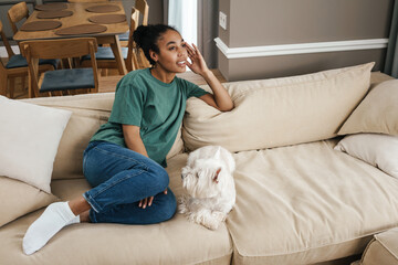 Happy black woman smiling and resting with her dog on sofa at home