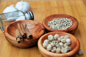 pepper, cardamom, and cinnamon in a wooden bowl on a wooden tray plus garlic and salt. close up with selective focus