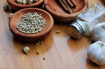 pepper, cardamom, and cinnamon in a wooden bowl on a wooden tray plus garlic and salt. close up with selective focus