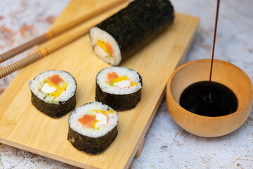 Sushi rolls with salmon avocado tuna and mango in a wood plate and stone texture background