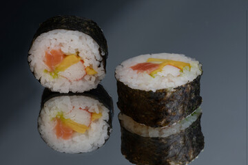 Sushi rolls with salmon avocado tuna and mango in a black background
