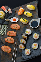 Sushi rolls nigiri, uramaki, hosomaki with salmon  and mango  with soy sauce in a black  stone background