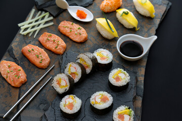 Sushi rolls nigiri, uramaki, hosomaki with salmon  and mango  with soy sauce in a black  stone background