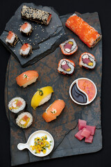 Sushi rolls nigiri, uramaki, hosomaki with salmon  and mango  with soy sauce in a black  stone background