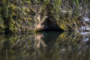 sandstone cliffs on the bank of a forest river with a perfect reflection in the water and green conifers on the bank.