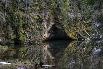 sandstone cliffs on the bank of a forest river with a perfect reflection in the water and green conifers on the bank.