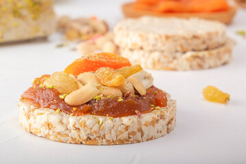 Puffed exploded wheat grains with peanuts and dried apricots on a thin layer of apricot jam on a background of oriental sweets on a white wooden table. Close-up