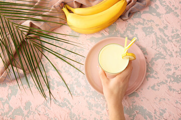 Female hand with glass of tasty banana milkshake on color background
