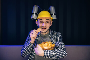 Caucasian man rests at home and watches TV shows or sports news on TV screen. Man with beer helmet...