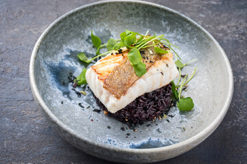Modern Style traditionelles gebratenes Skrei Kabeljau Fisch Filet mit Portulaca Salat und schwarzen Reis serviert als close-up auf einem Nordic Design Teller mit Textfreiraum