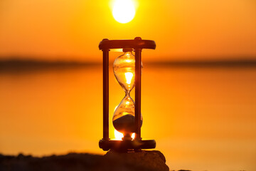 Stylish hourglass on sand near river outdoors