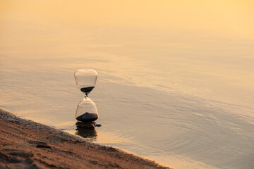 Stylish hourglass near river at sunset